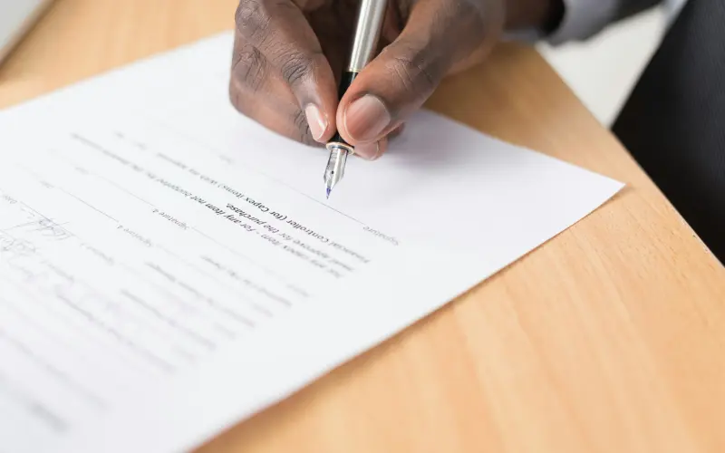 Person signing a document with a pen